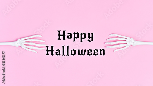 Happy Halloween text with scary skeleton hands on pastel pink background. Flat lay