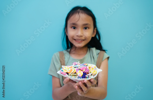 Child holding candy , jelly in hand Little asian girl eating candy.blow with colorful candies in the hands of little girl.