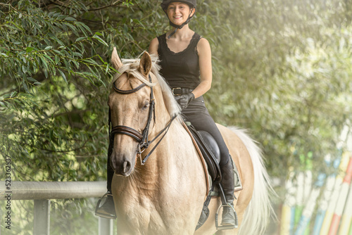 Portrait of a young woman riding a palomino kinsky warmblood horse in summer outdoors. Equestrian riding scene