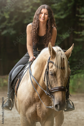 Portrait of a young woman riding a palomino kinsky warmblood horse in summer outdoors. Equestrian riding scene © Annabell Gsödl