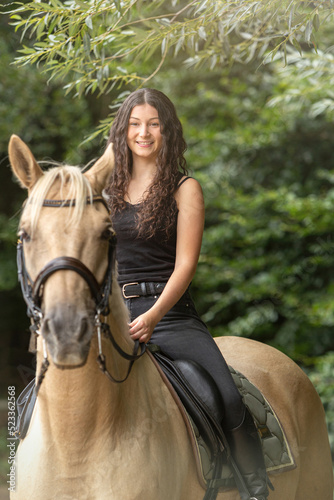 Portrait of a young woman riding a palomino kinsky warmblood horse in summer outdoors. Equestrian riding scene photo