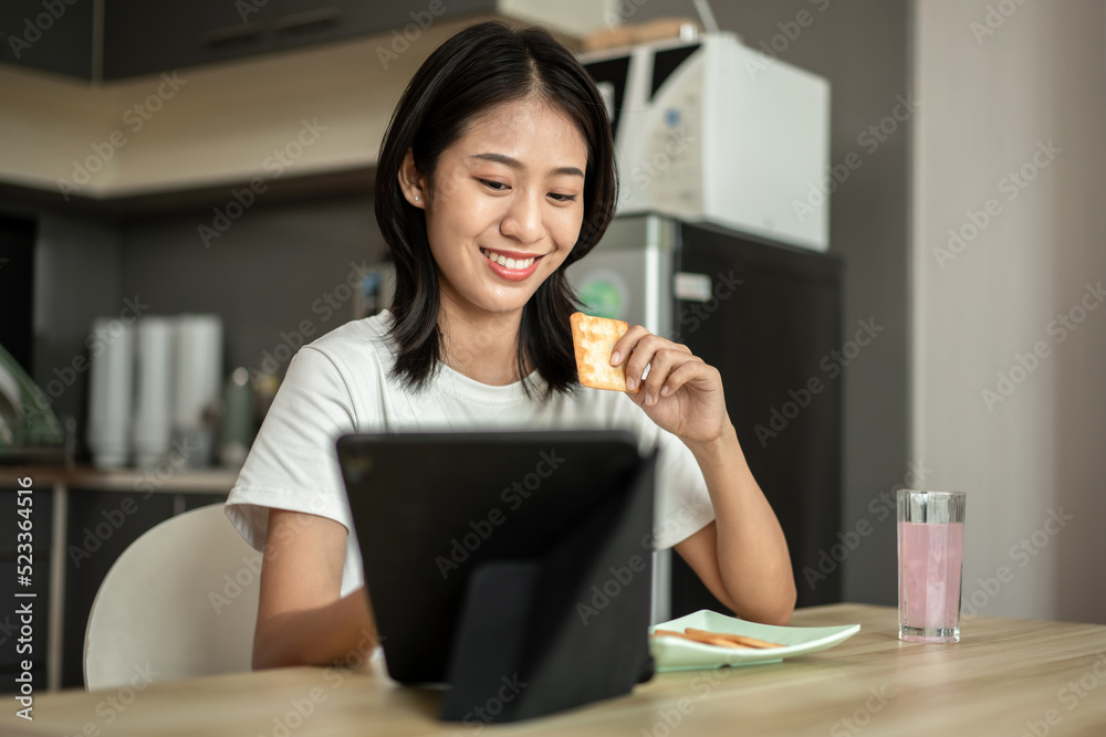 Woman is having breakfast with crackers mixed with various grains and using tablets to update her morning news, Small room in condominium background, Wake-up activities Woman is having breakfast with crackers mixed with various grains and using tablets to update her morning news, Small room in condominium background, Wake-up activities