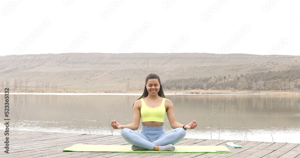 American black sportswoman sitting on lake enjoying fresh air meditating for zen, healthcare. Motivation. Active lifestyle.