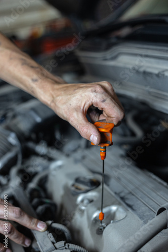 A male mechanic checks the oil level in the car engine in close-up. The mechanic holds a dipstick in his hand to check the oil level in the car.Focus on hand with yellow oil gage. © Dmitry Presnyakov