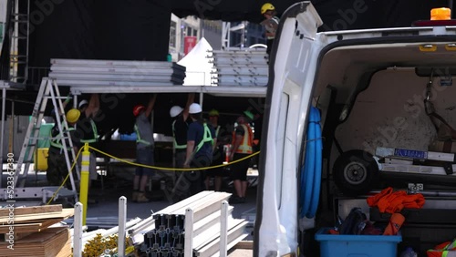 Short selective focus video on a street in Montreal as blurry construction workers are seen erecting scaffolding behind a van filled with work tools.