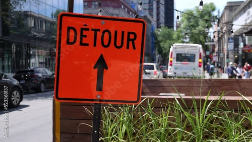 Closeup slow mo video of an orange detour sign on a busy road in Montreal, Canada. City center traffic is seen queuing in background with copy space. photo