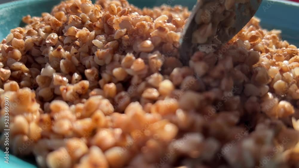 Cooked buckwheat stirring with a spoon on the blue dish, eco cereal mixing process, ready organic food on the plate. Cooked buckwheat stirring with a spoon on the blue dish, eco cereal mixing process, ready organic food on the plate.