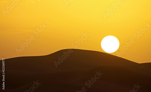 Gold yellow sunset with circular full round sun ball over silhouette of desert sand dunes sky - Morocco, Erg Chebbi, North Africa