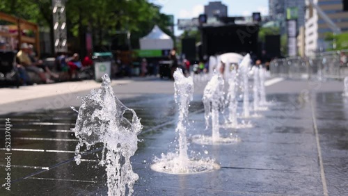 Slow mo selective focus clip of splash fountain water jets spraying out of sidewalk in city center of Montreal, Canada during summer. With copy space.