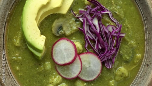 Green Pozole Verde dish with hominy, tomatillo, shredded jackfruit and button mushrooms with avocado, radish and red cabbage. Close-up of vegan pozole dish. photo