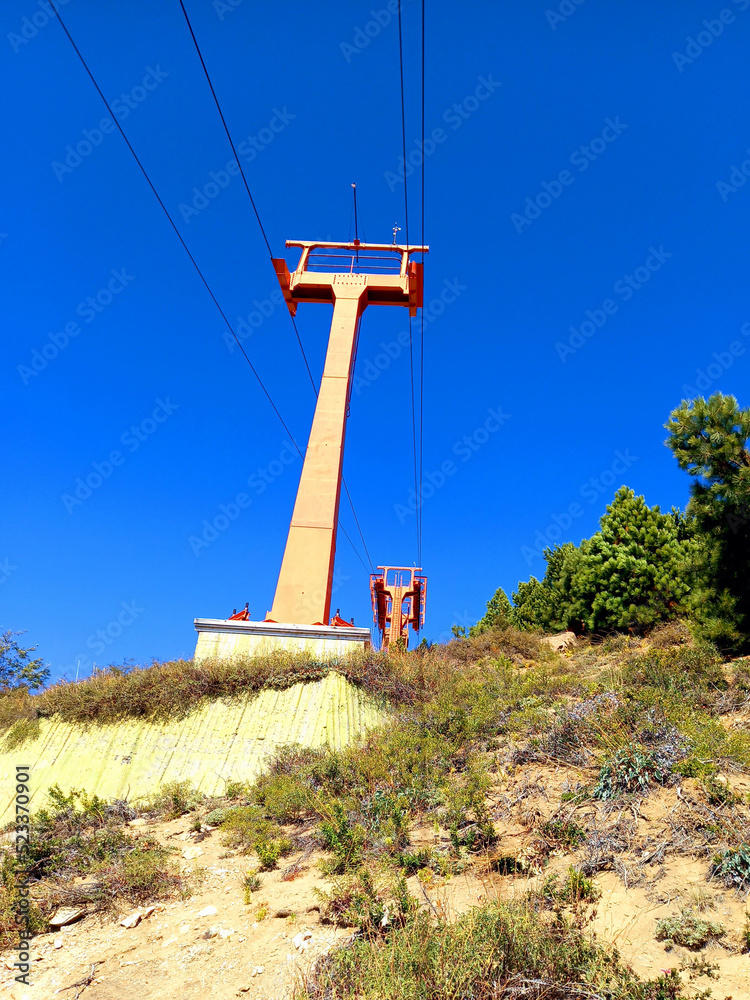 View from below of ski lift on Escape Mountain under blue sky. Constructions and engineering. Wiring and power lines for chair lifts and mountain lifts. View from below of ski lift on Escape Mountain under blue sky. Constructions and engineering. Wiring and power lines for chair lifts and mountain lifts.