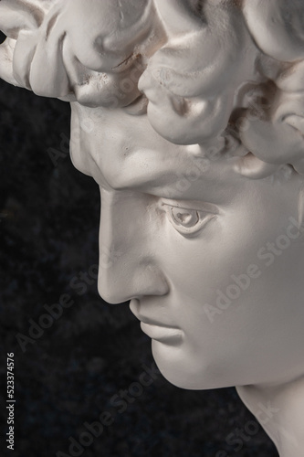 Gypsum copy of head statue David for artists on dark background. Replica of face famous sculpture youth of David by Michelangelo. Template design for art, dj, fashion, poster, zine. Renaissance epoch.