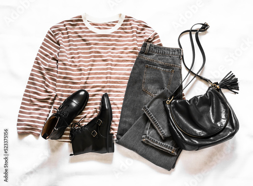 Grey jeans, black leather shoes, black leather bag, long sleeve striped t-shirt - women's clothing on a light background, top view. Fashion concept