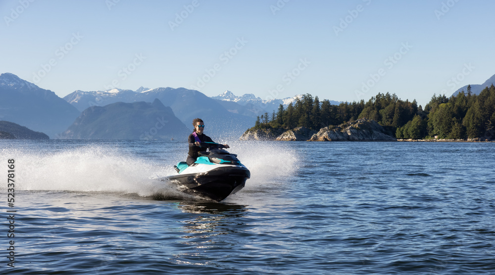 Fototapeta premium Adventurous Caucasian Woman on Water Scooter riding in the Ocean. Howe Sound and mountain landscape in background. West Vancouver, British Columbia, Canada.