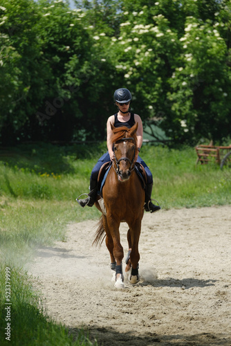 The girl with black helmet riding a sorrel horse at a riding school
