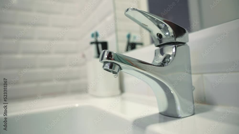 Water leak concept. Static video of a silver faucet in a bathroom with dripping water. Faucet malfunction, drops of clean water dripping into the white washbasin Water leak concept. Static video of a silver faucet in a bathroom with dripping water. Faucet malfunction, drops of clean water dripping into the white washbasin