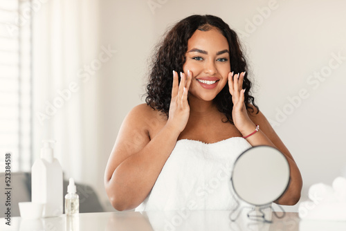 Tableau sur toile Beautiful black plus size woman in towel making face-lifting massage, sitting at