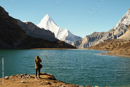 asian photographer taking a photo of the holy mount jampayang and lake boyongcuo in yading national park, china