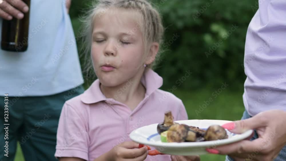 Close-up. little girl takes bite and eats baked red pepper with pleasure. Barbecue grill party in nature outside. Having picnic with friends. good company of friends Close-up. little girl takes bite and eats baked red pepper with pleasure. Barbecue grill party in nature outside. Having picnic with friends. good company of friends