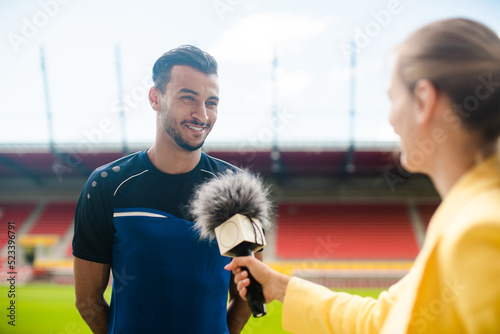 Reporter interviewing football player in a stadium holding microphone in hand