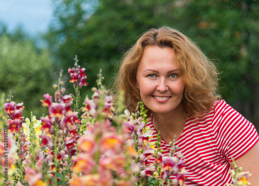 a girl with red curly hair in a red dress on a background of flowers in the garden and greenery. a girl with red curly hair in a red dress on a background of flowers in the garden and greenery.