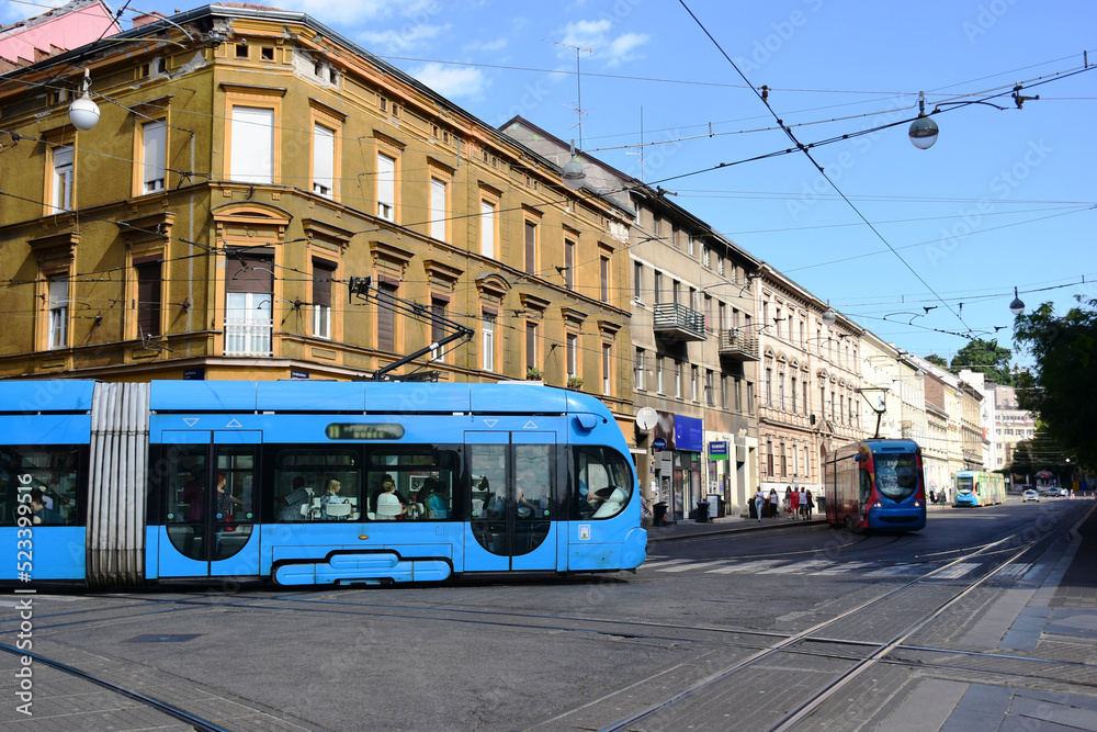 Fototapeta premium modern blue tram side perspective view in Zagreb, Croatia. major street in downtown. old classic residential buildings and stucco facades in the background. travel and tourism concept. urban scene.