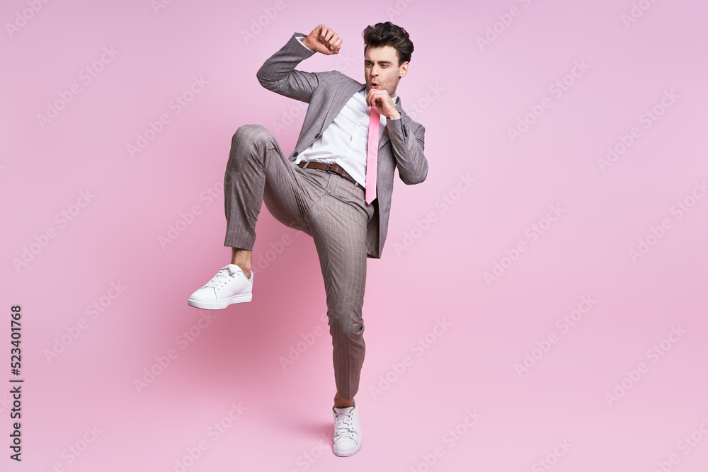 Furious young man in full suit fighting while standing against pink background Furious young man in full suit fighting while standing against pink background