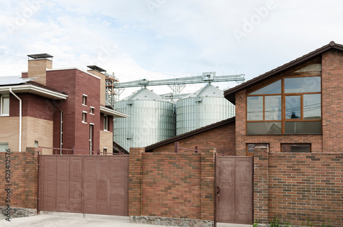 Modern Granary elevator near town houses. Silver silos on agro-processing and manufacturing plant for processing drying cleaning and storage of agricultural products, flour, cereals and grain.