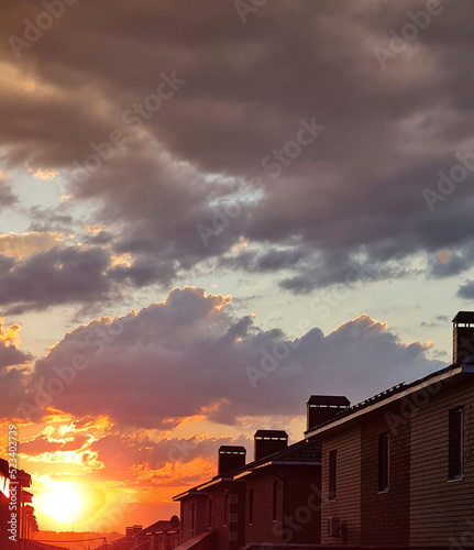 bright sunset,orange,red end of the day rays of the departing sun between the houses in the village with a chimney on the roof,against a beautiful sky with clouds