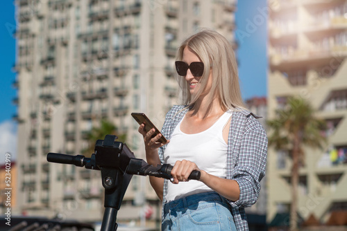 Wallpaper Mural Young smiling blonde woman in sunglasses unlocks an electric scooter with a mobile phone on a sunny day, copy space Torontodigital.ca