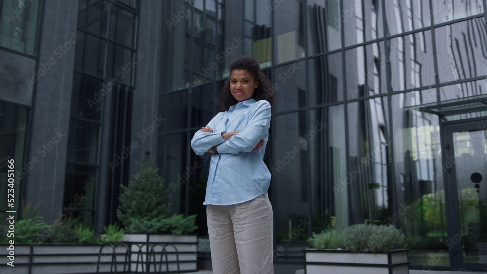 Cheerful manager standing at office building alone. Content businesswoman smile