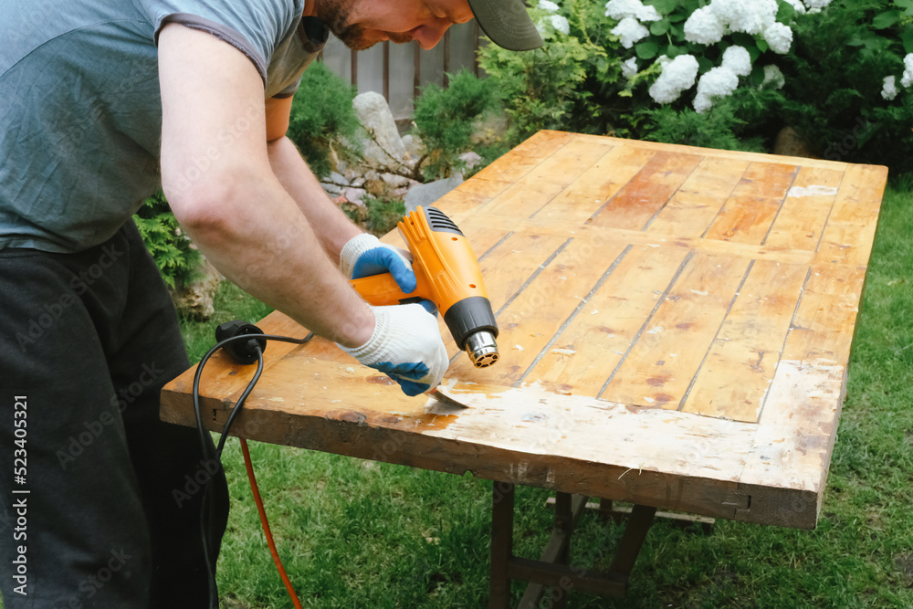 Man removing old varnish and paint from wood using scraper and heat gun.  Restoration work of old wooden table outdoors. Furniture repair, reuse of  old things concept. Stock Photo | Adobe Stock