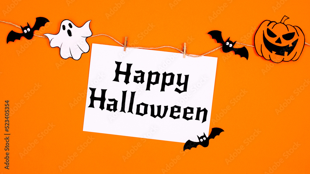 Creative paper card with Happy Halloween hanged on rope with scary stickers for Halloween on orange background. Flat lay