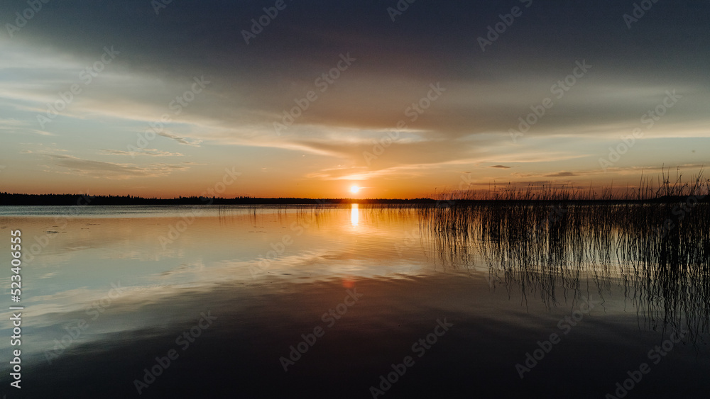 Obraz premium Sunset reflecting in the water with reeds and the horizon in the distance over Candle Lake in Northern Saskatchewan, Canada