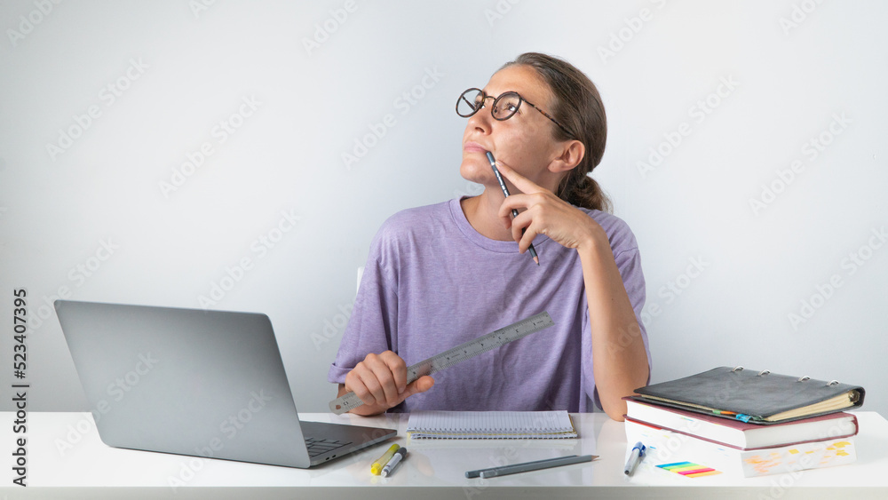 A girl with a laptop with a pile of books and notebooks on the table with a pensive look A girl with a laptop with a pile of books and notebooks on the table with a pensive look