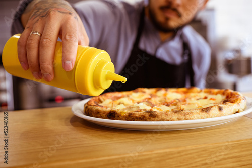 Partial view of tattooed chef pouring olive oil on delicious pizza in cafe
