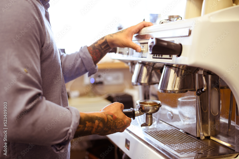 Faceless view of tattooed barista holding holder and using coffee machine in cafe Faceless view of tattooed barista holding holder and using coffee machine in cafe