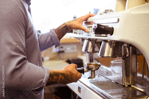 Faceless view of tattooed barista holding holder and using coffee machine in cafe