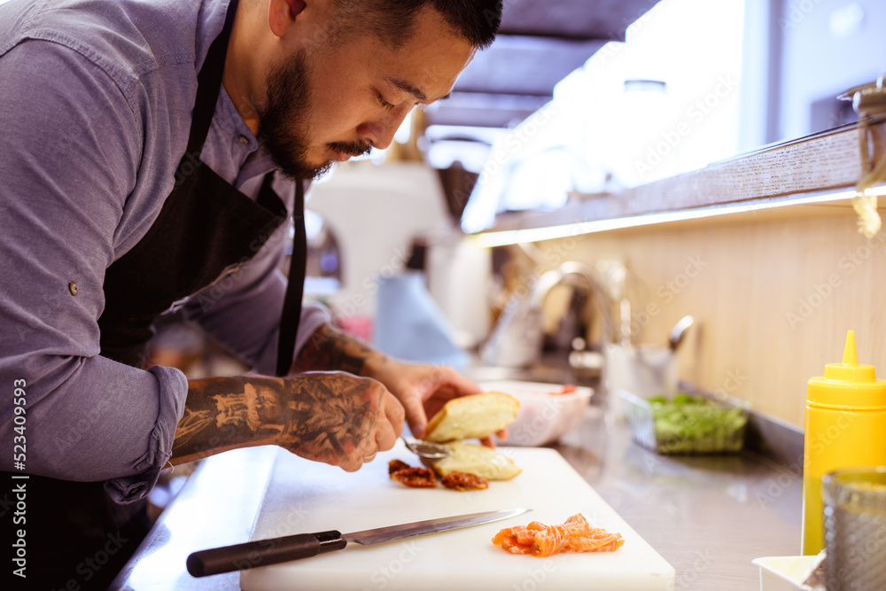 Asian chef preparing ciabatta with salmon in cafe kitchen 