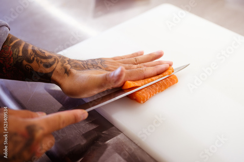 Faceless shot of tattooed chef cutting salmon in restaurant kitchen 