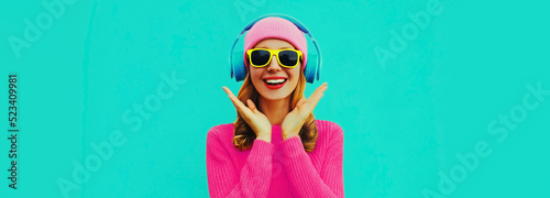 Portrait of happy surprised smiling young woman model with headphones listening to music wearing colorful sweater on blue background
