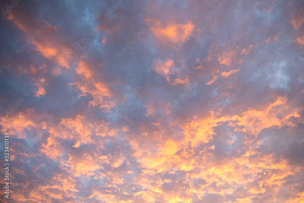 Bright orange rays of sunset sun illuminate clouds in blue evening sky
