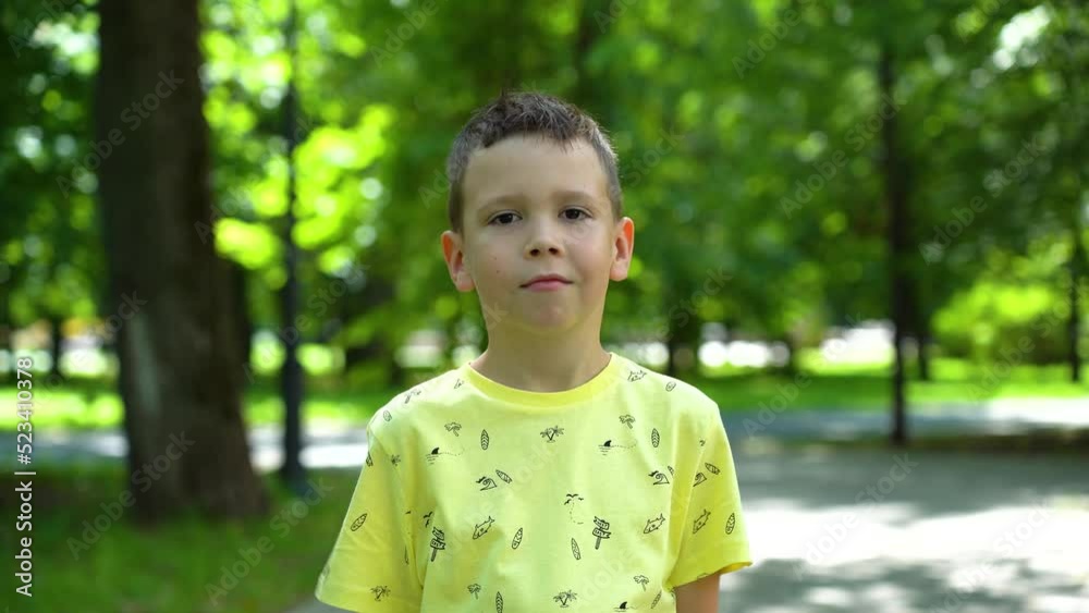 Caucasian boy showing class gestures on a sunny summer day in a green park under the trees. The boy shows gestures with his fingers cool in the park among the green trees in the background