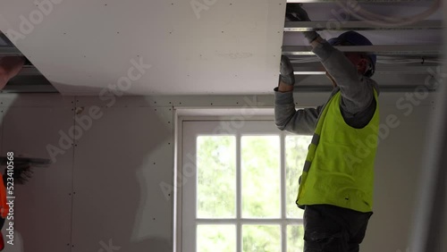 Hard male work on construction site. Two professional workers in special uniforms Contractors Safety Hats repairing ceiling wall inside building. Builders' equipment at workplace. industrial premises photo