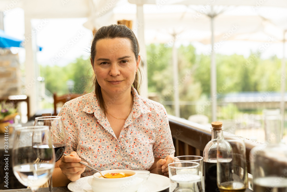 Positive woman eating tomato soup Gazpacho with bread served with glass of wine at restaurant