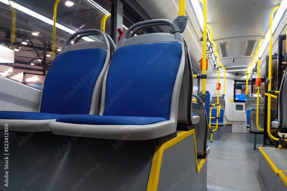 Passenger bus inside view. City passenger transport. Big bus with blue seats. Validators for fare payment on handrails. City transport interior. New bus without anyone. Urban passenger infrastructure