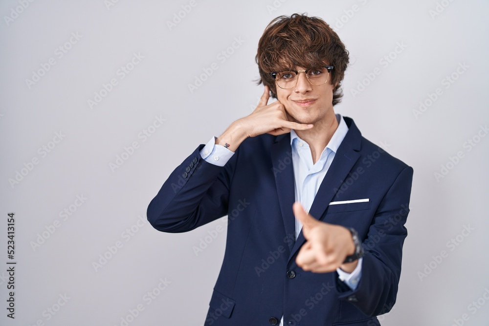 Hispanic business young man wearing glasses smiling doing talking on the telephone gesture and pointing to you. call me. Hispanic business young man wearing glasses smiling doing talking on the telephone gesture and pointing to you. call me.