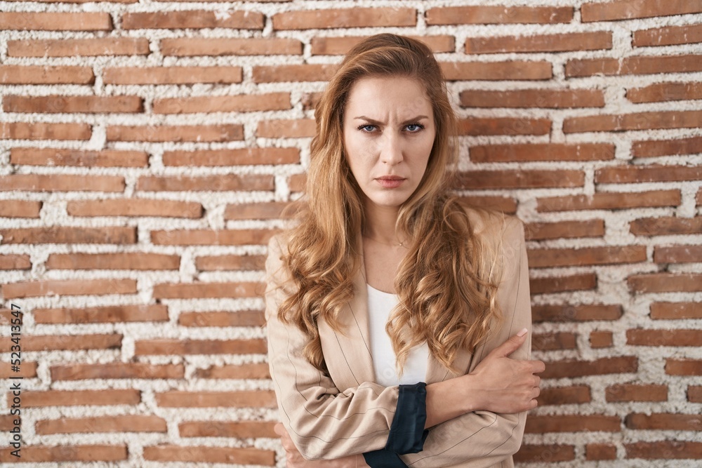 Beautiful blonde woman standing over bricks wall skeptic and nervous, disapproving expression on face with crossed arms. negative person.