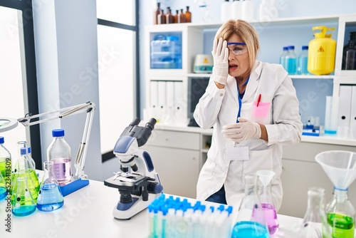 Middle age blonde woman working at scientist laboratory yawning tired covering half face  eye and mouth with hand. face hurts in pain.