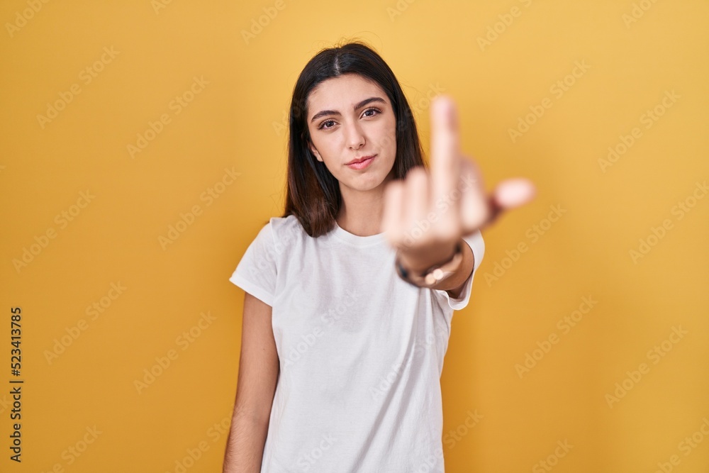 Young beautiful woman standing over yellow background showing middle finger, impolite and rude fuck off expression Young beautiful woman standing over yellow background showing middle finger, impolite and rude fuck off expression